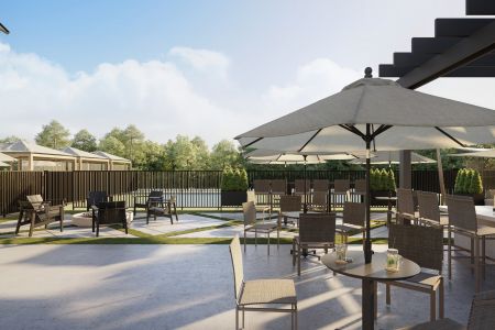 Outdoor patio with tables, chairs, and umbrellas, overlooking a fenced green area with trees and a bright, partly cloudy sky.