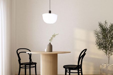 Minimalist dining area with round wooden table, two black chairs, a pendant light, and a potted plant.