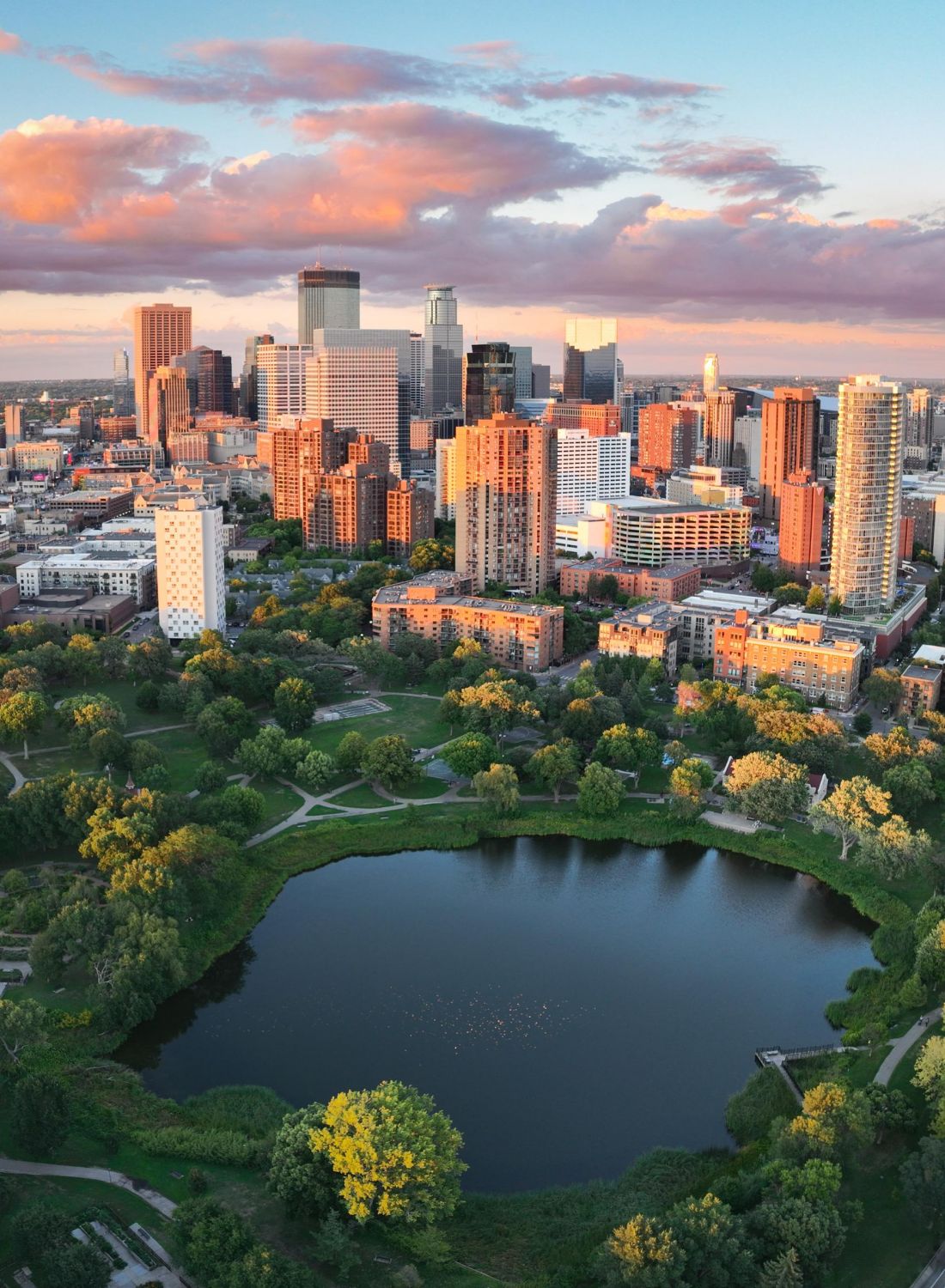 Aerial view of a city skyline at sunset with a round lake and green park in the foreground.